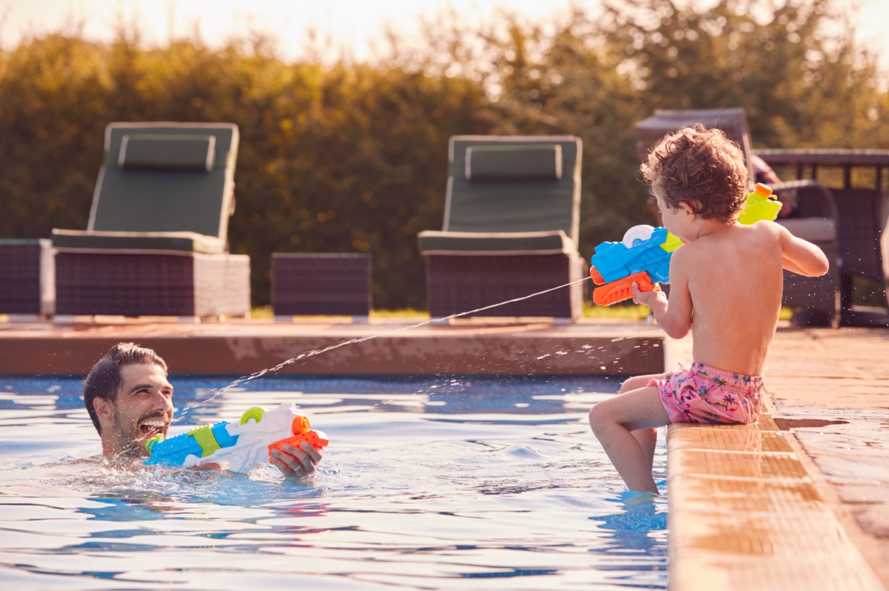 An adult and child playing with Super Soaker water blasters in a pool, showing how the concept evolved into a popular product.